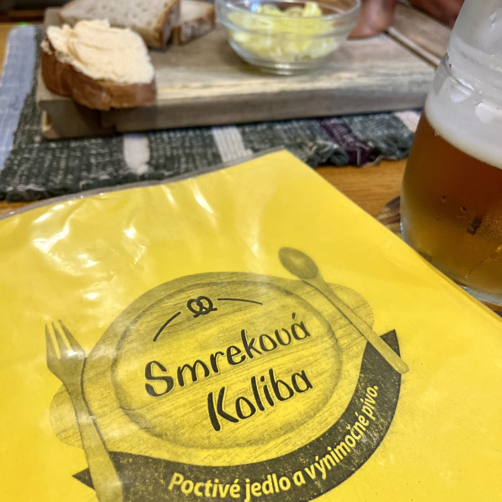 Yellow package with 'Smrekova Koliba' branding, bread, butter, and a glass of beer on a table.